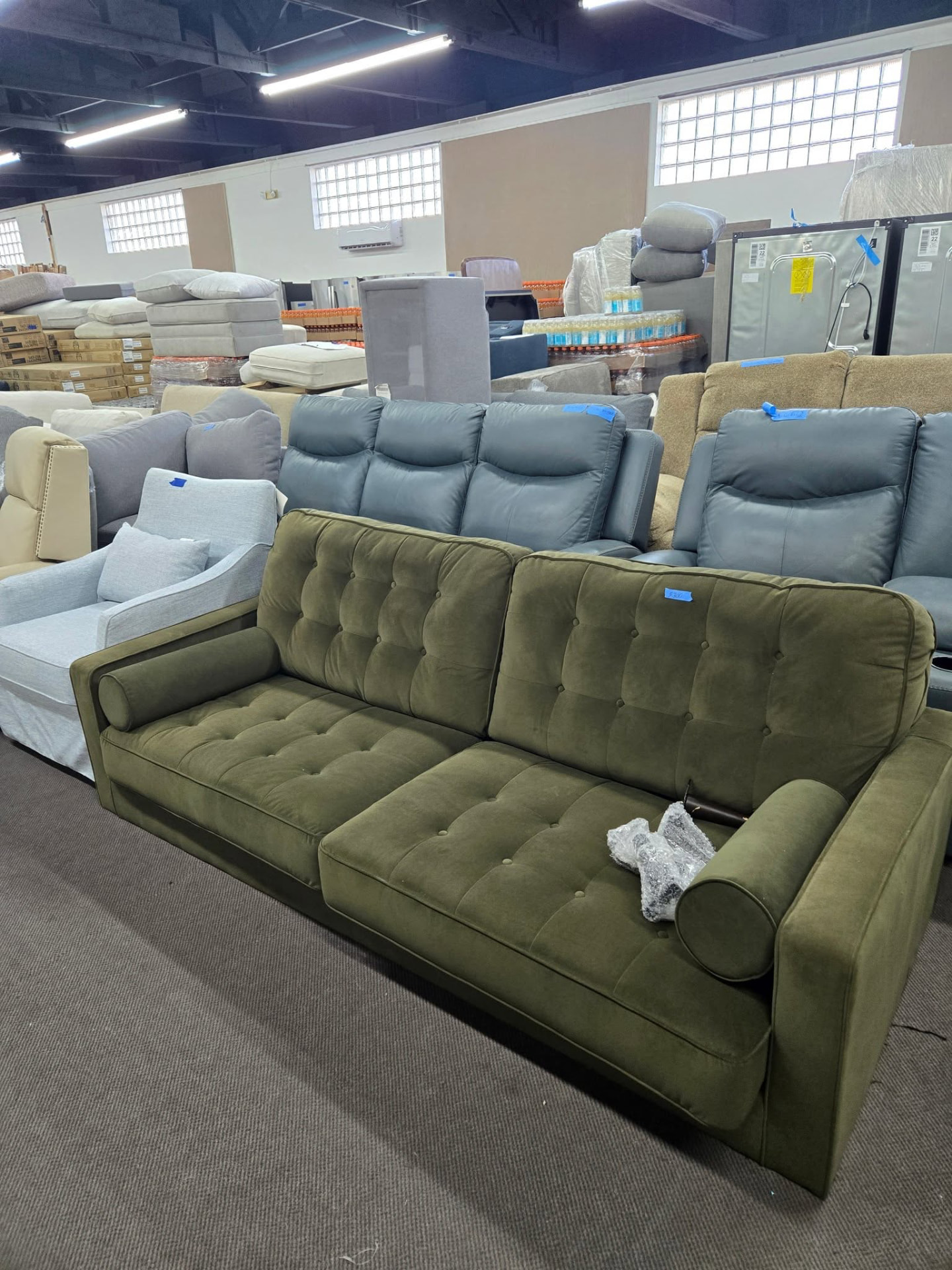 Green tufted sofa among rows of couches in the warehouse